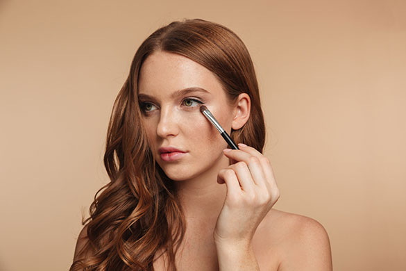 Woman applying makeup on lower eyelid with brush