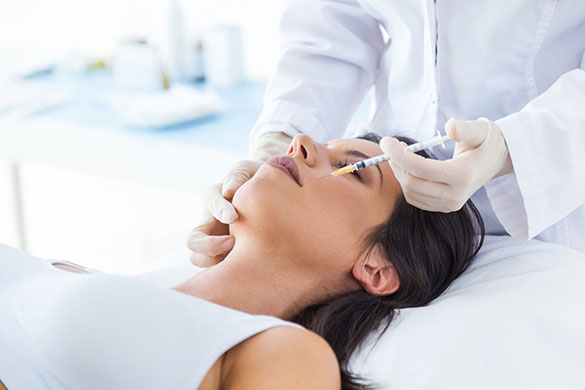 Woman lying down on clinic bed receiving dermal filler treatment