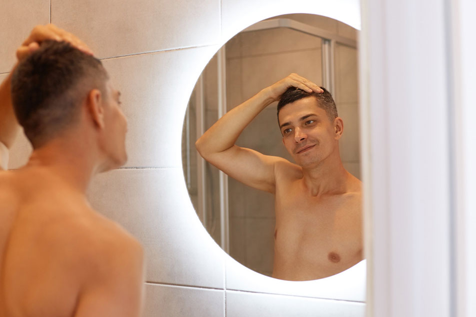 Man smiling and holding his hair while looking at himself in the bathroom mirror