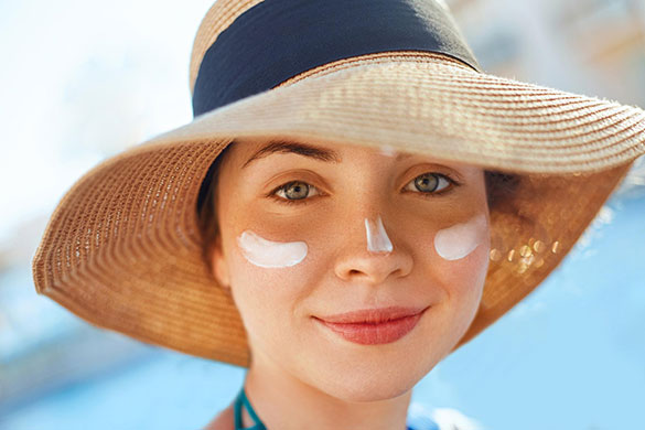 Smiling woman wearing sunhat with sunscreen smeared on her face