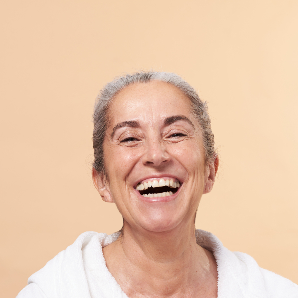 grey haired women with fine lines laughing on a beige background