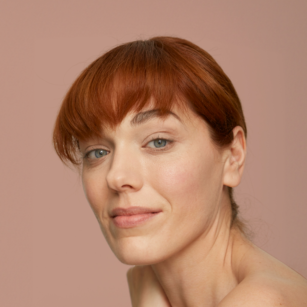 closeup of women with red hair smiling on a blush background