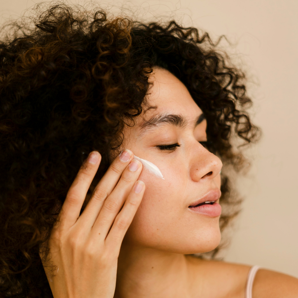Side profile of a women applying skincare on a beige background