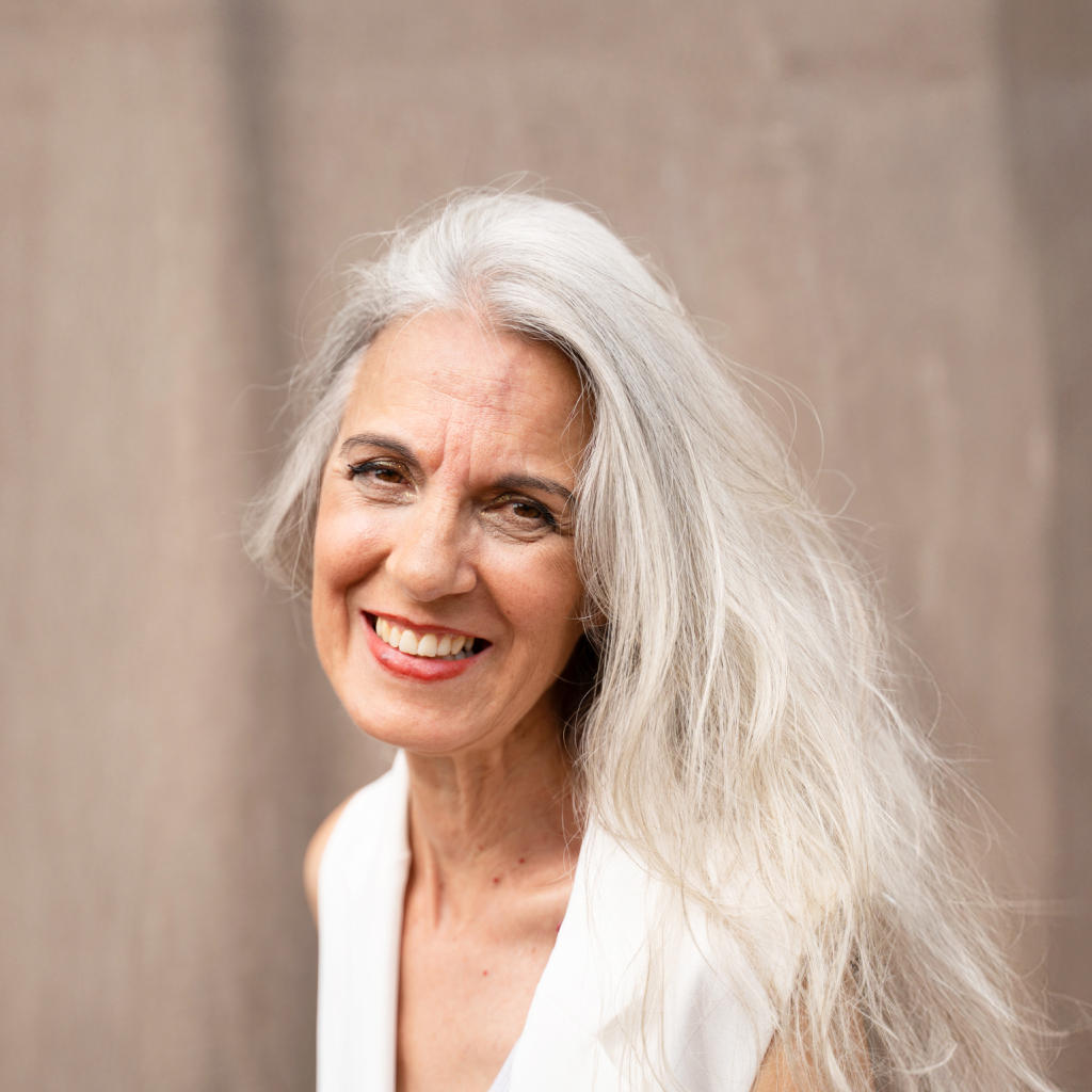 Portrait of an older woman with long white hair wearing a white top.