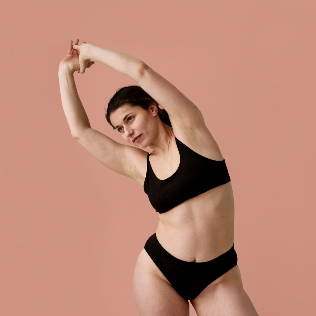 women in black under garments stretching against blush background