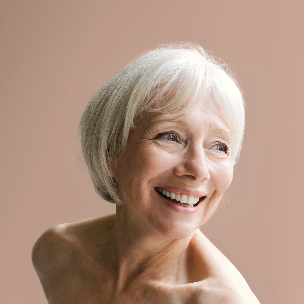 closeup of short haired middle age women with grey hair smiling on a beige background