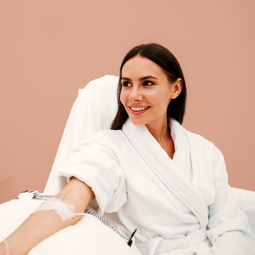 women with her arm extended recieving an IV on a blush background