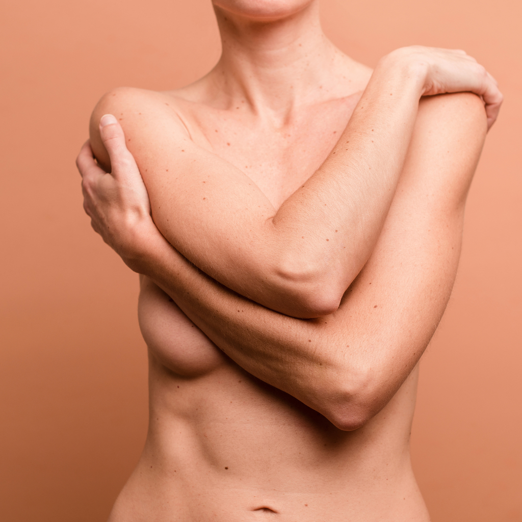 picture of a nude women's chest with her arms crossed covering her breasts on a brown background