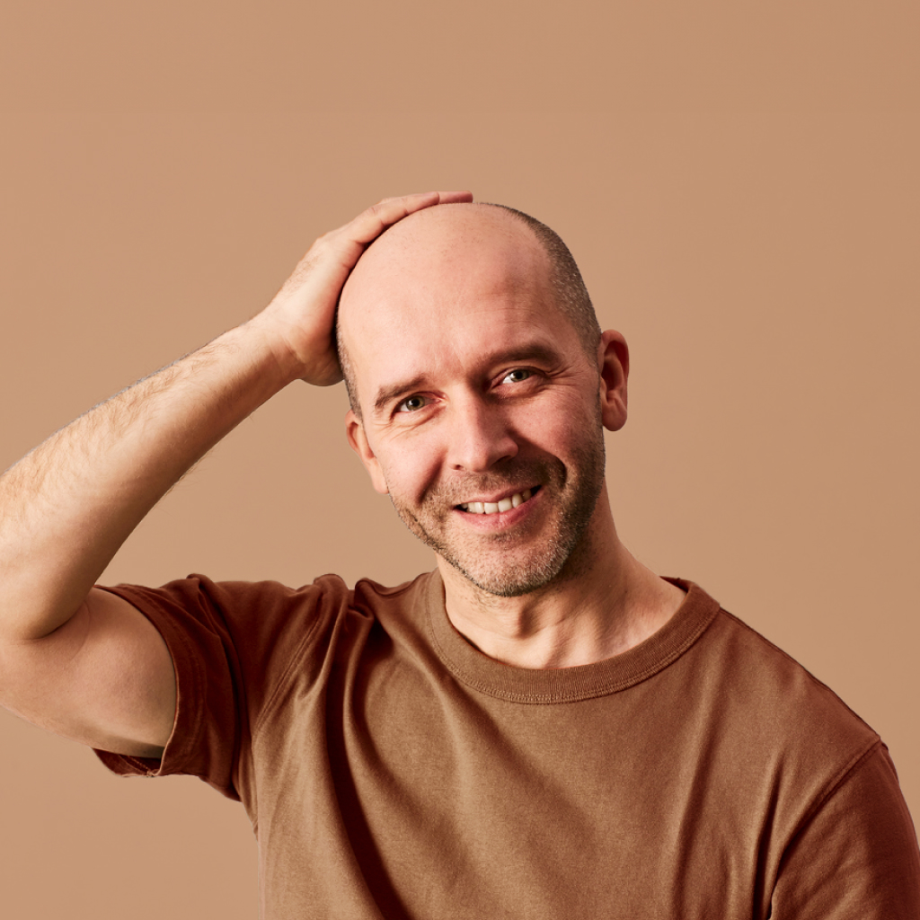 bald man touching head on a brown background
