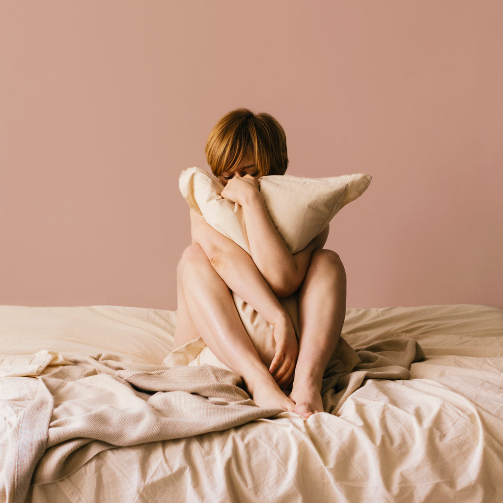 person clutching pillow on a bed on a pink background
