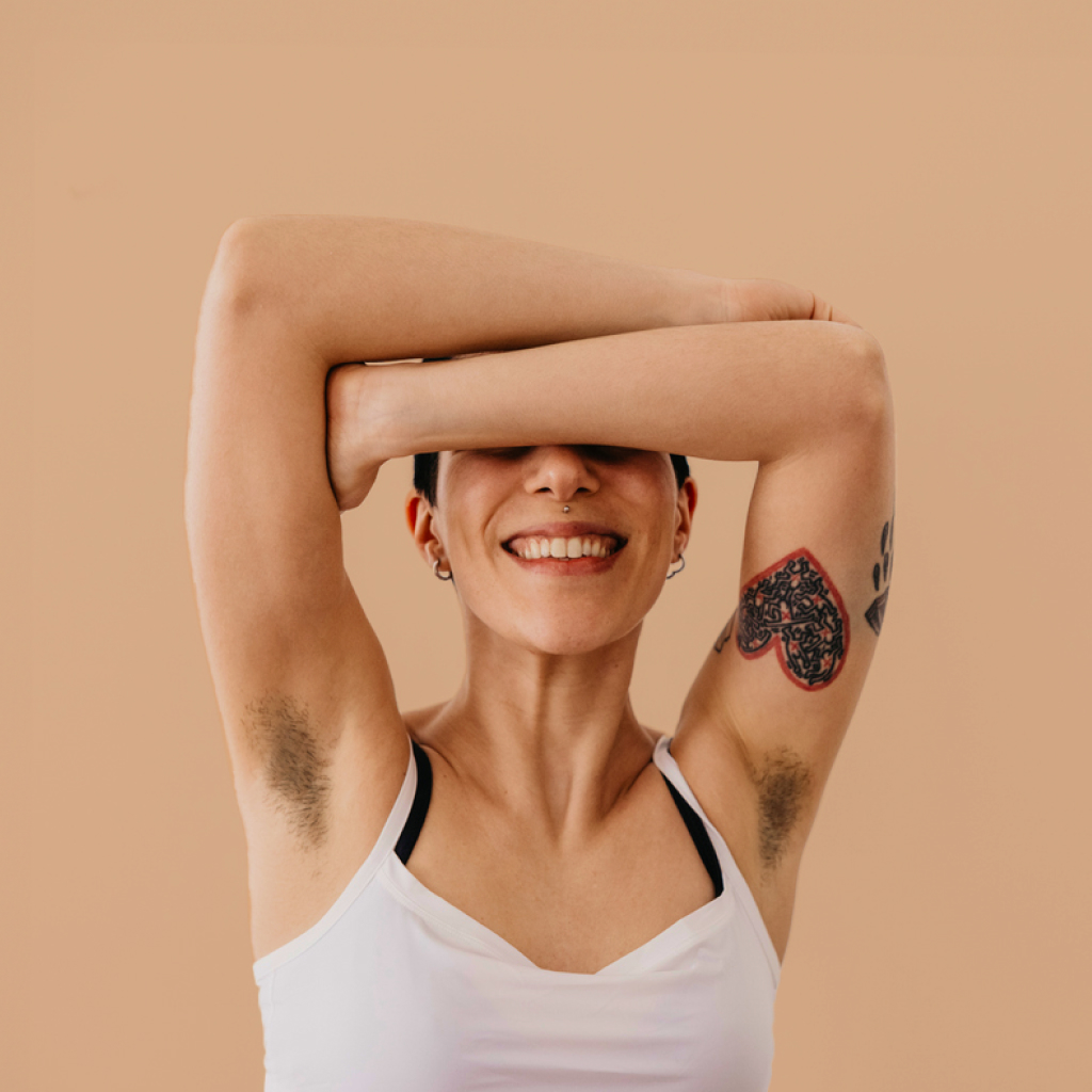 person with their arms raised above their head revealing hairy under arms on a beige background