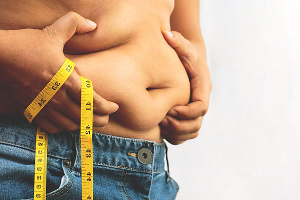 Man in jeans pinching his tummy fat with measuring tape wrapped around his hand