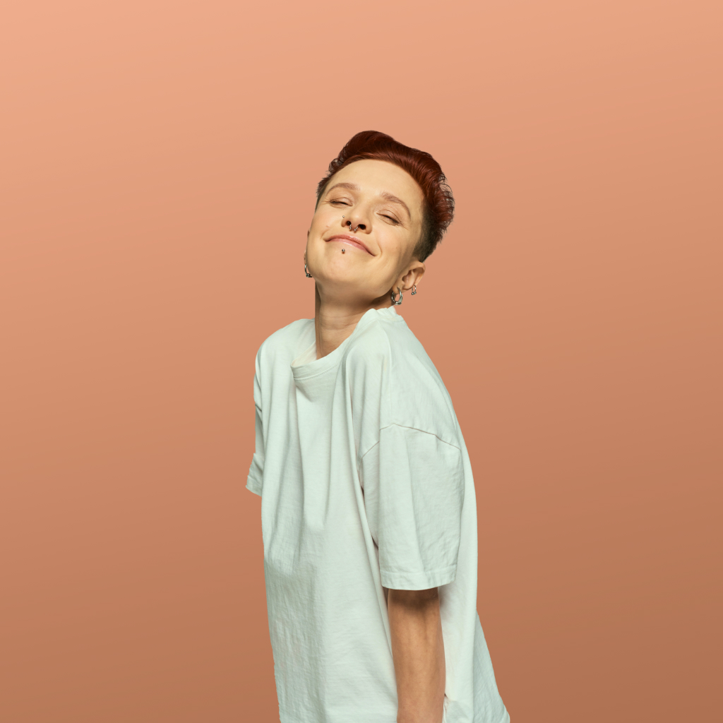 person wearing a long white shirt smiling on a peach background
